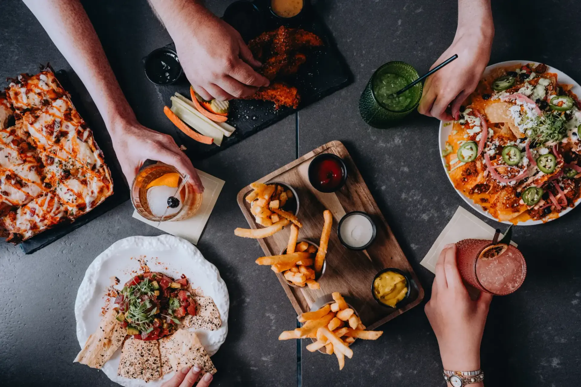Overhead view of a group sharing scratch-kitchen plates and cocktails